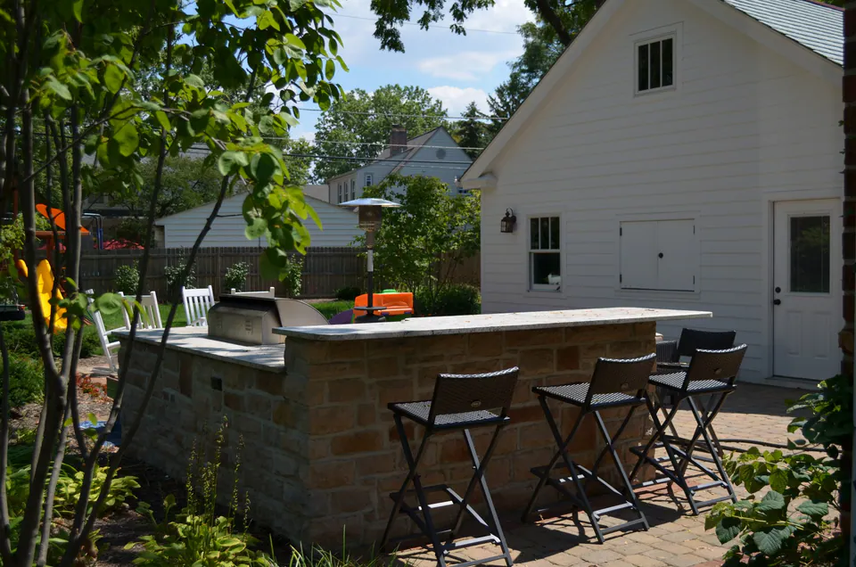 L-shaped stone bar counter with a built-in grill and bar stools on a paver patio